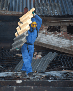 Travailleur en tenue de protection complète manipulant un matériau contenant de l’amiante lors d’une opération de décontamination.