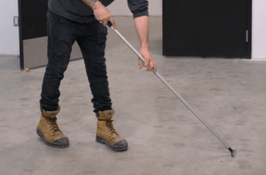 Travailleur retirant des résidus de colle sur un plancher à l’aide d’un grattoir après des travaux de construction.